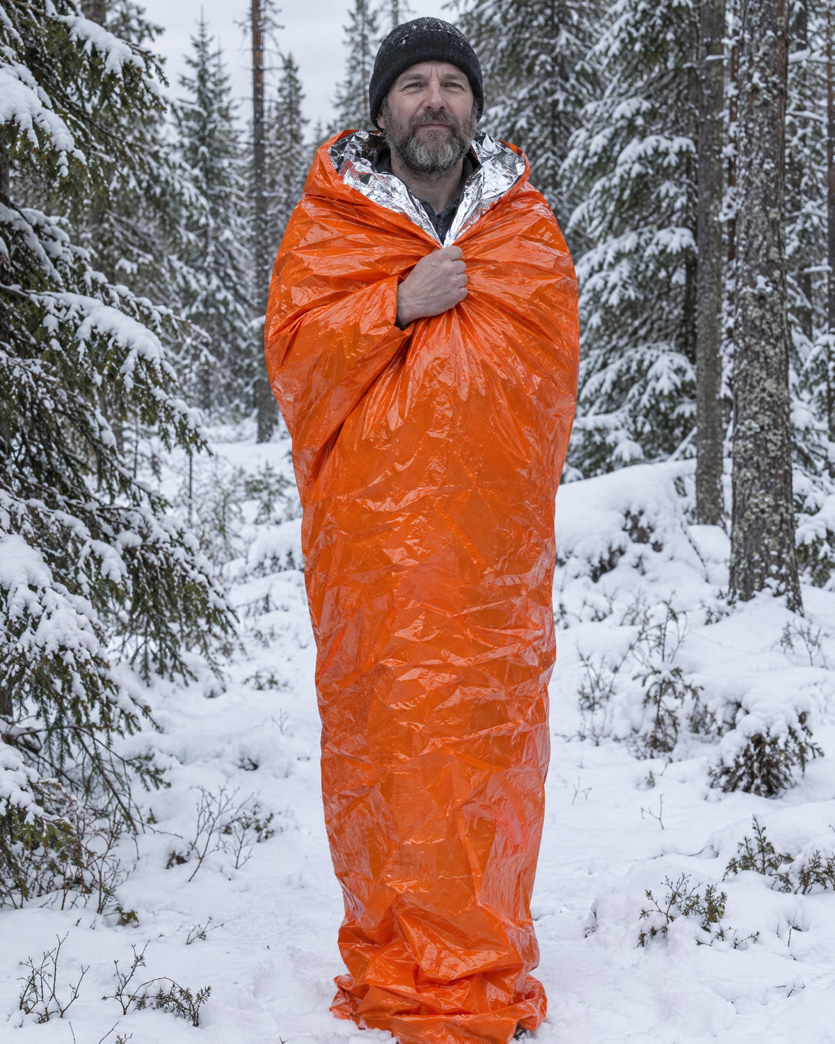 Man i nödsovsäck i snöig skog